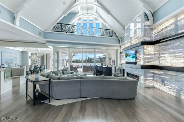 living room with a chandelier, high vaulted ceiling, a lit fireplace, and wood finished floors