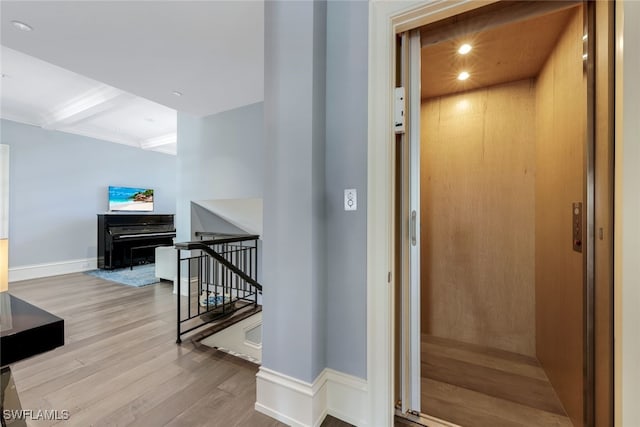 stairway with hardwood / wood-style flooring, beamed ceiling, and elevator