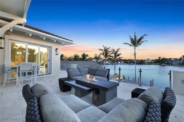 patio terrace at dusk with a water view, a dock, and an outdoor fire pit