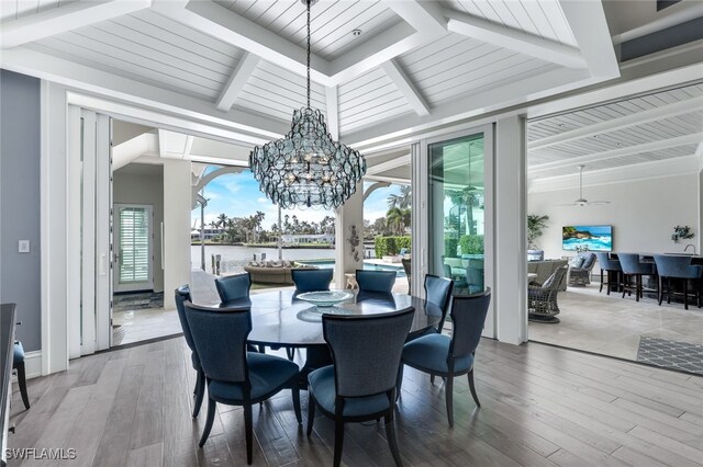 dining room with ceiling fan with notable chandelier, a water view, wood finished floors, and beam ceiling