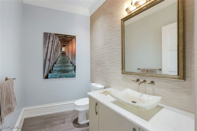 bathroom featuring baseboards, toilet, wood finished floors, crown molding, and vanity