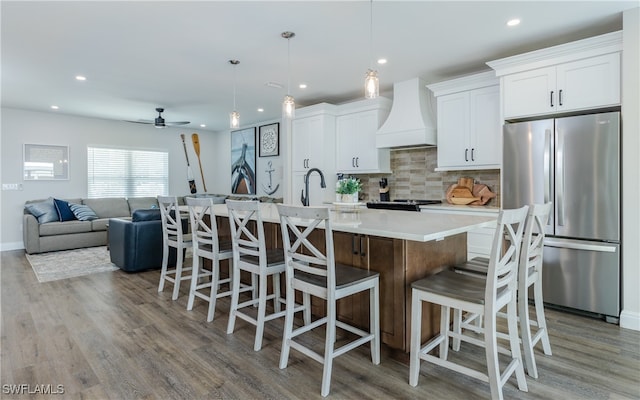 kitchen featuring a large island, stainless steel fridge, white cabinetry, and custom range hood