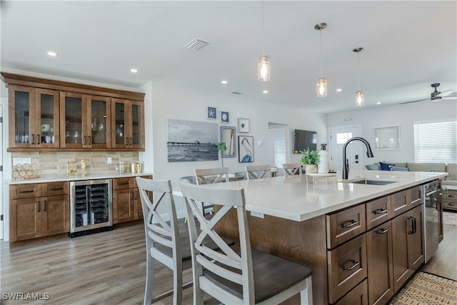 kitchen with sink, a kitchen breakfast bar, light hardwood / wood-style floors, wine cooler, and a center island with sink