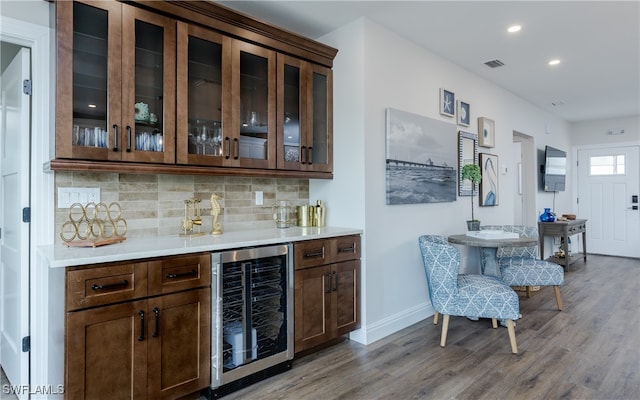 bar featuring wine cooler, tasteful backsplash, dark brown cabinets, and hardwood / wood-style floors