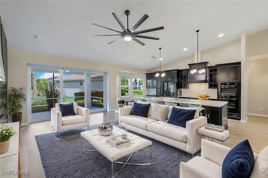 living room with ceiling fan, sink, vaulted ceiling, and light wood-type flooring