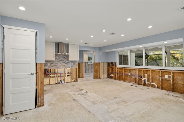 kitchen featuring white cabinets, wall chimney range hood, and tasteful backsplash