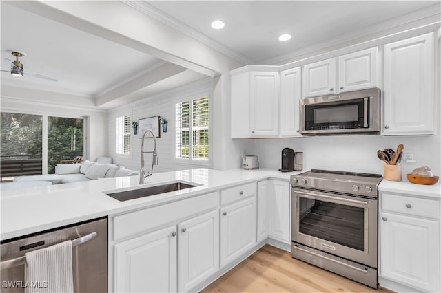 kitchen featuring appliances with stainless steel finishes, sink, white cabinets, ornamental molding, and kitchen peninsula