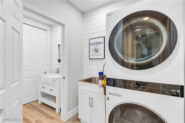 laundry room with cabinets, stacked washer and dryer, light hardwood / wood-style flooring, and sink