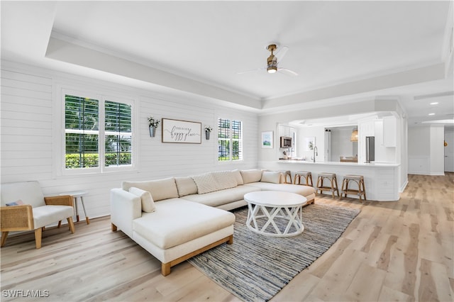 living room with a tray ceiling, sink, ceiling fan, light hardwood / wood-style floors, and crown molding