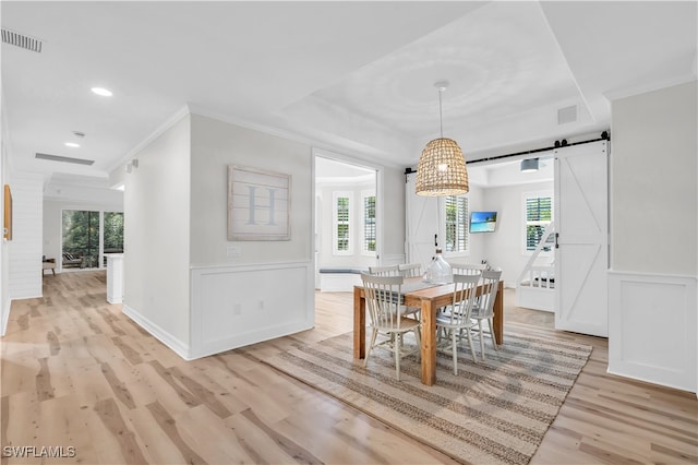 dining space featuring crown molding, a barn door, plenty of natural light, and light hardwood / wood-style flooring