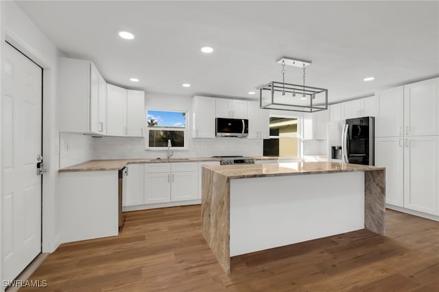 kitchen with appliances with stainless steel finishes, light hardwood / wood-style flooring, a kitchen island, and white cabinets