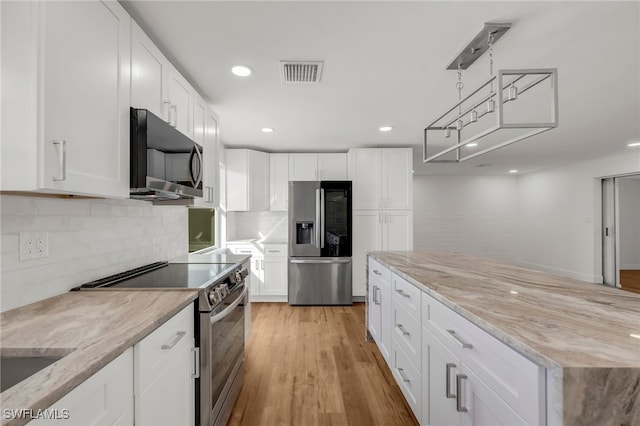 kitchen featuring light stone countertops, appliances with stainless steel finishes, white cabinetry, and light hardwood / wood-style floors