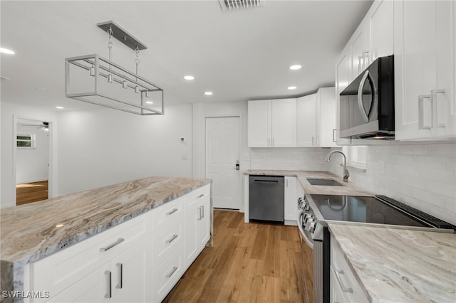 kitchen featuring appliances with stainless steel finishes, sink, light wood-type flooring, hanging light fixtures, and white cabinets