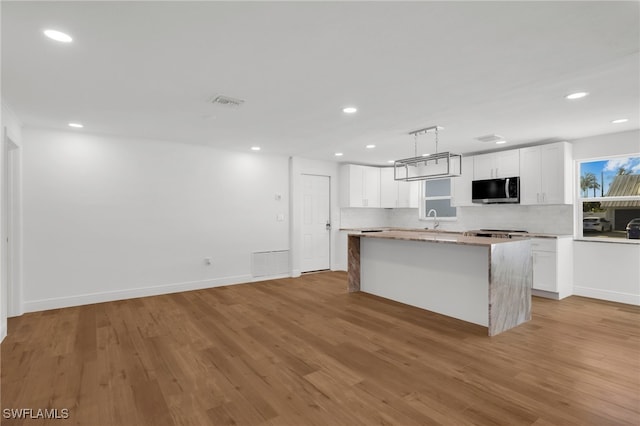 kitchen with white cabinets, a kitchen island, light wood-type flooring, sink, and decorative light fixtures