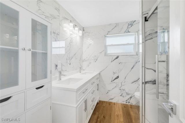 bathroom with wood-type flooring, tile walls, toilet, tiled shower, and vanity