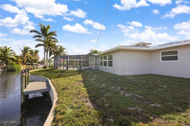 view of yard with a boat dock, a water view, and glass enclosure