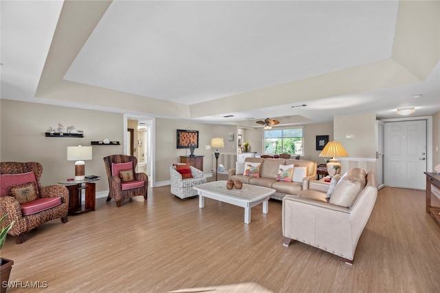 living room with a tray ceiling, light wood-type flooring, and ceiling fan