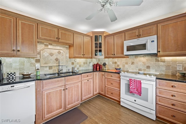 kitchen featuring backsplash, hardwood / wood-style flooring, dark stone countertops, sink, and white appliances