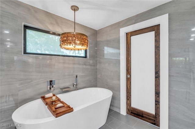 bathroom featuring a notable chandelier, a tub to relax in, tile walls, and tile patterned flooring