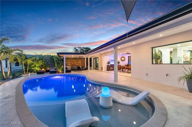 pool at dusk with a patio and an outdoor living space