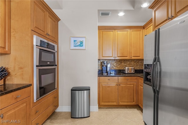 kitchen featuring decorative backsplash, appliances with stainless steel finishes, light tile patterned floors, and dark stone countertops