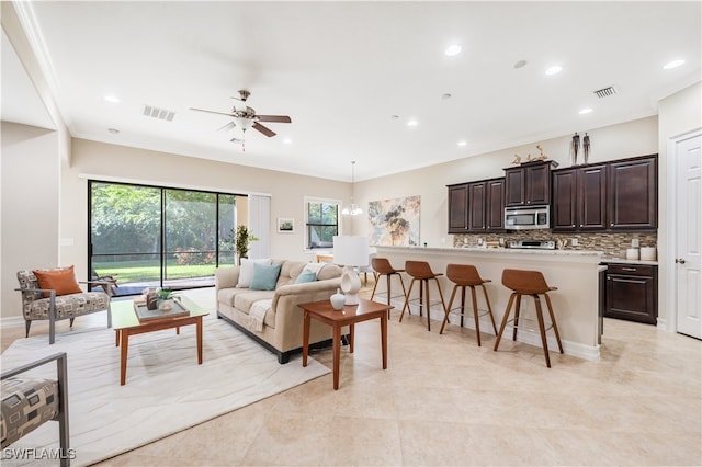 living room with crown molding, light tile patterned floors, and ceiling fan with notable chandelier