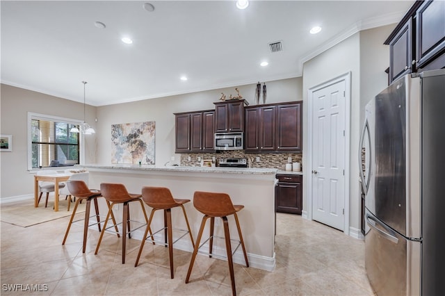 kitchen with appliances with stainless steel finishes, a breakfast bar, an island with sink, and hanging light fixtures