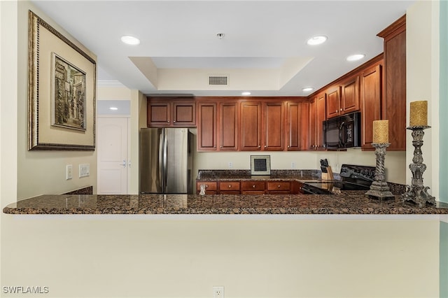 kitchen featuring dark stone counters, black appliances, a tray ceiling, and kitchen peninsula