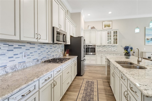 kitchen with appliances with stainless steel finishes, sink, light wood-type flooring, hanging light fixtures, and decorative backsplash