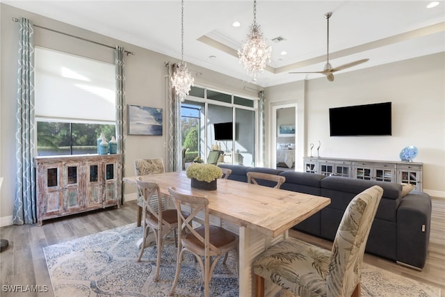 dining space with crown molding, wood-type flooring, ceiling fan with notable chandelier, and a raised ceiling