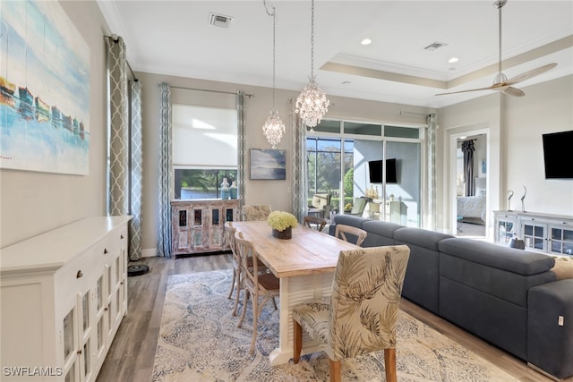 dining area featuring crown molding, hardwood / wood-style flooring, a tray ceiling, and ceiling fan with notable chandelier