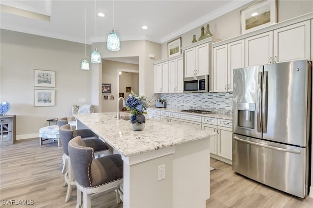 kitchen with white cabinets, light stone counters, stainless steel appliances, and a kitchen island with sink