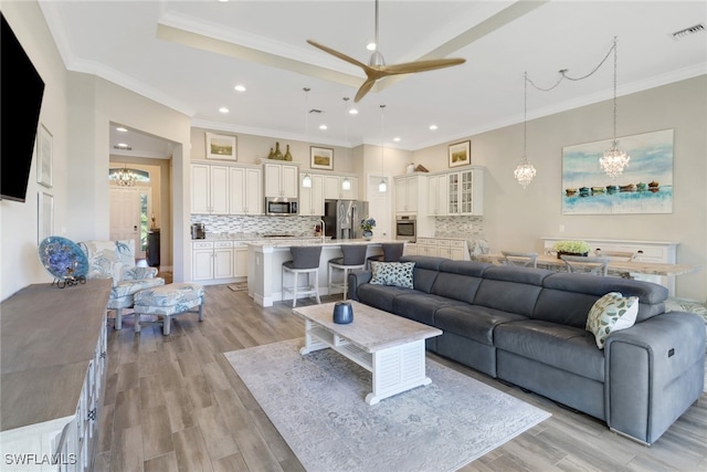 living room with light hardwood / wood-style flooring, ceiling fan with notable chandelier, and crown molding