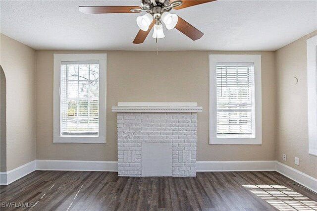 unfurnished living room featuring dark wood-type flooring, ceiling fan, a textured ceiling, and a fireplace