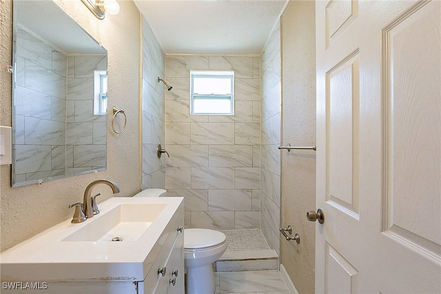 bathroom featuring vanity, a tile shower, and toilet