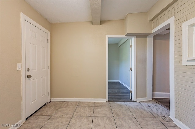 corridor with brick wall, a textured ceiling, and light tile patterned floors