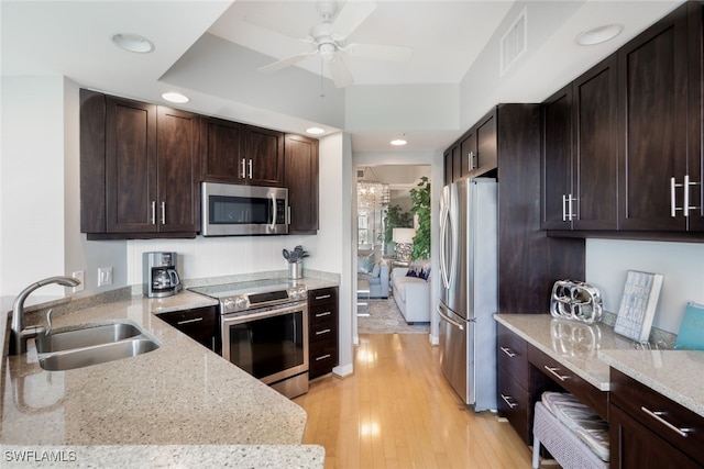 kitchen featuring stainless steel appliances, sink, light wood-type flooring, light stone counters, and ceiling fan