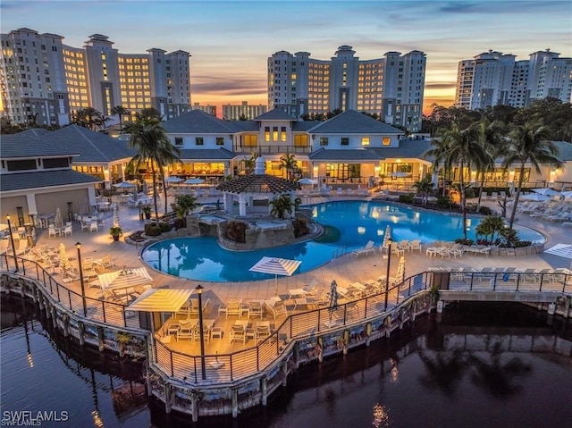 pool at dusk with a hot tub and a patio area