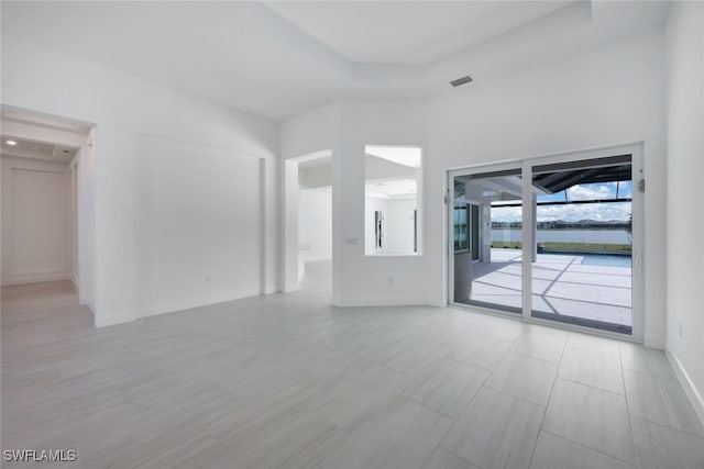 unfurnished living room with a tray ceiling, visible vents, a towering ceiling, and baseboards