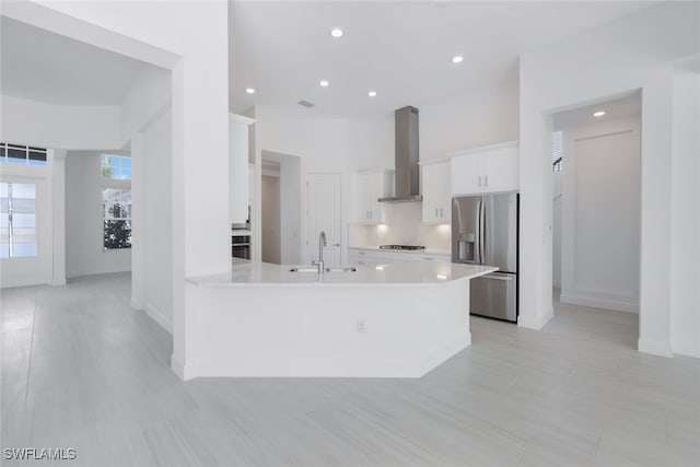 kitchen with stainless steel appliances, light countertops, white cabinetry, a sink, and wall chimney range hood