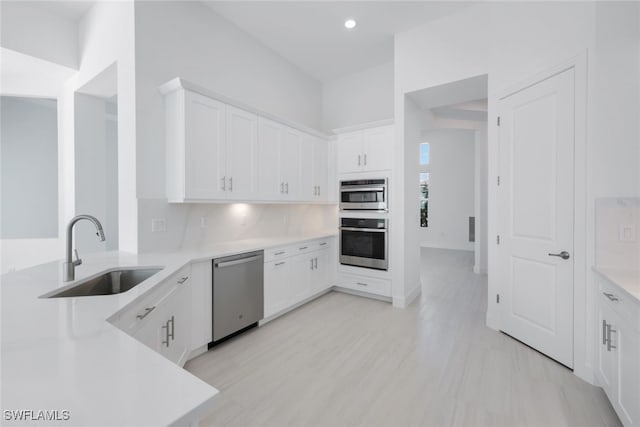 kitchen with white cabinets, stainless steel appliances, light countertops, and a sink