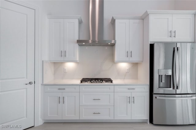 kitchen with stainless steel appliances, wall chimney range hood, decorative backsplash, and white cabinets