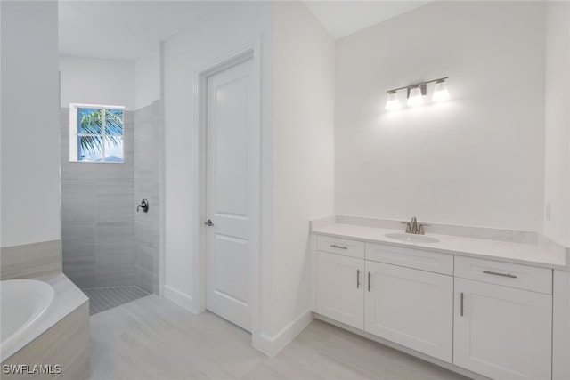 bathroom featuring tiled shower, vanity, baseboards, and a bath