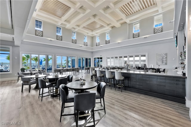 dining room featuring beamed ceiling, coffered ceiling, light hardwood / wood-style flooring, and a towering ceiling