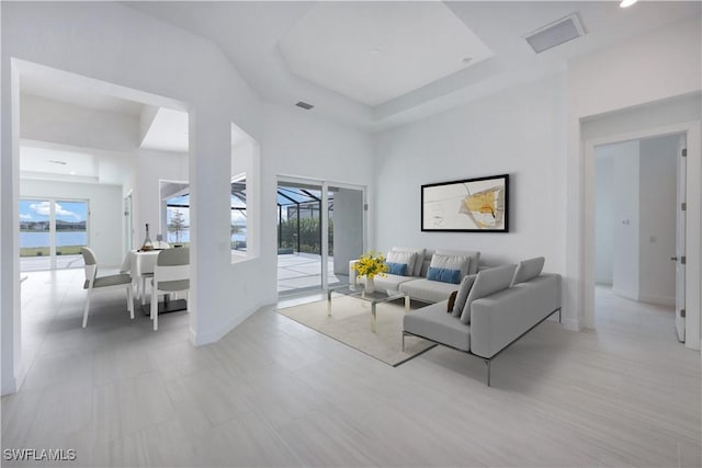 living area featuring a high ceiling, a raised ceiling, visible vents, and baseboards