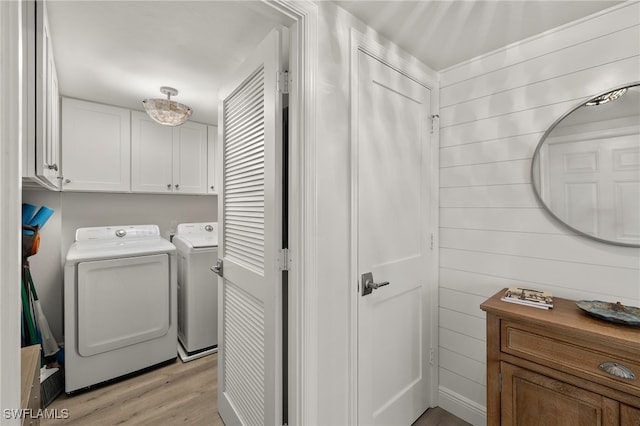 clothes washing area with washing machine and clothes dryer, wooden walls, cabinets, and light wood-type flooring