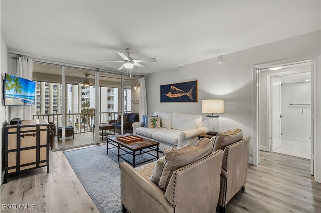 living room with ceiling fan, light hardwood / wood-style floors, and a wall of windows