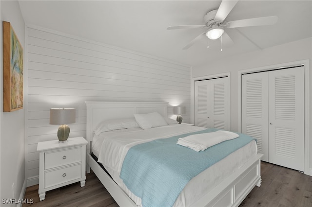 bedroom with ceiling fan, wood walls, dark hardwood / wood-style flooring, and multiple closets