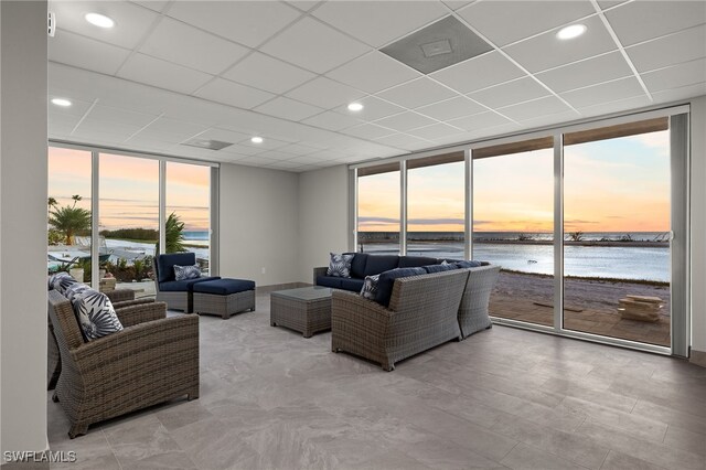 living room featuring expansive windows, a drop ceiling, and a water view