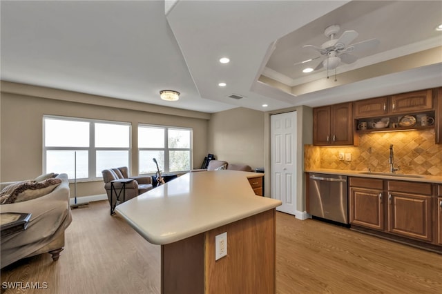 kitchen featuring a kitchen island, a sink, light countertops, stainless steel dishwasher, and a raised ceiling